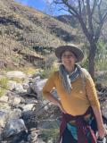 Photo of Anisa Kline in a desert setting in front of a large hill. 