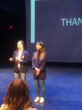 two women on stage with the back of someone's head in the foreground.