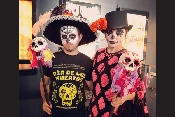 A man has a skull painted on her face and a woman is wearing a top hat with a skull painted on her face