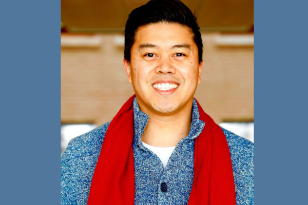 An asian man smiling and wearing a bright red scarf