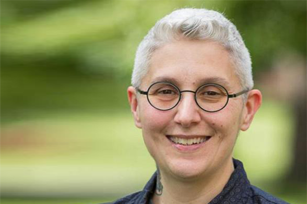 Photo of a woman with short grey hair and round glasses, smiling