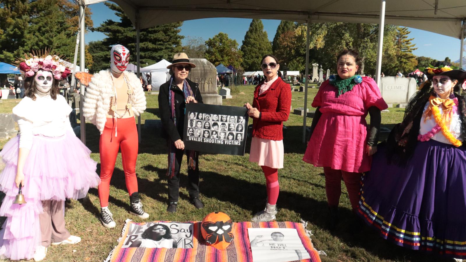 Six people standing around a picnic blanket, dressed in Day of the Dead costumes
