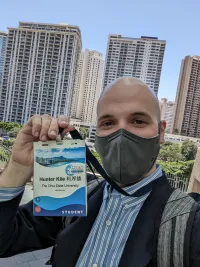 A man wearing a mask, holding up a conference badge